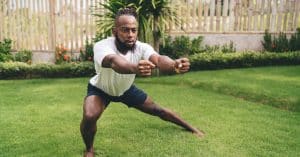 A man in a T-shirt and shorts exercising without equipment in an outdoor area full of lush green grass.