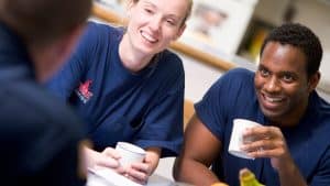 Firefighters sitting around a table smiling, holding cups, and talking. A bowl of fruit sits on the table in front of them.