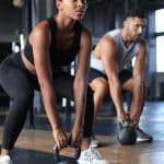 A woman and a man are working out in a private gym. The woman is using a kettlebell and is squatting.