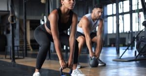 A woman and a man are working out in a private gym. The woman is using a kettlebell and is squatting.