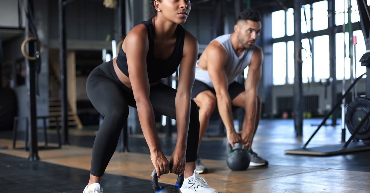 A woman and a man are working out in a private gym. The woman is using a kettlebell and is squatting.