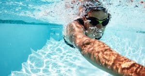 A person wearing a pair of black and green goggles swims beneath the surface of the water in a pool.