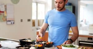 A man with brown hair and a beard portions healthy meals into plastic containers at a kitchen counter.