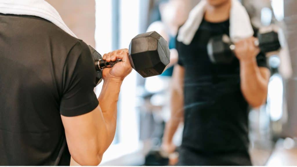 Crop man working out in front of a mirror with weights in gym