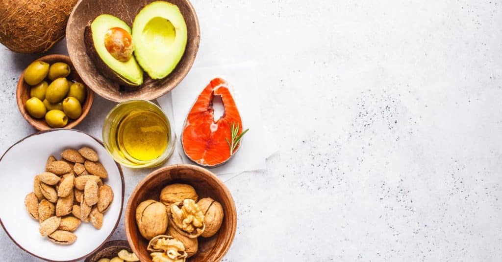 An assortment of foods known for their healthy fat contents, including nuts, oil, fruits, and fish.
