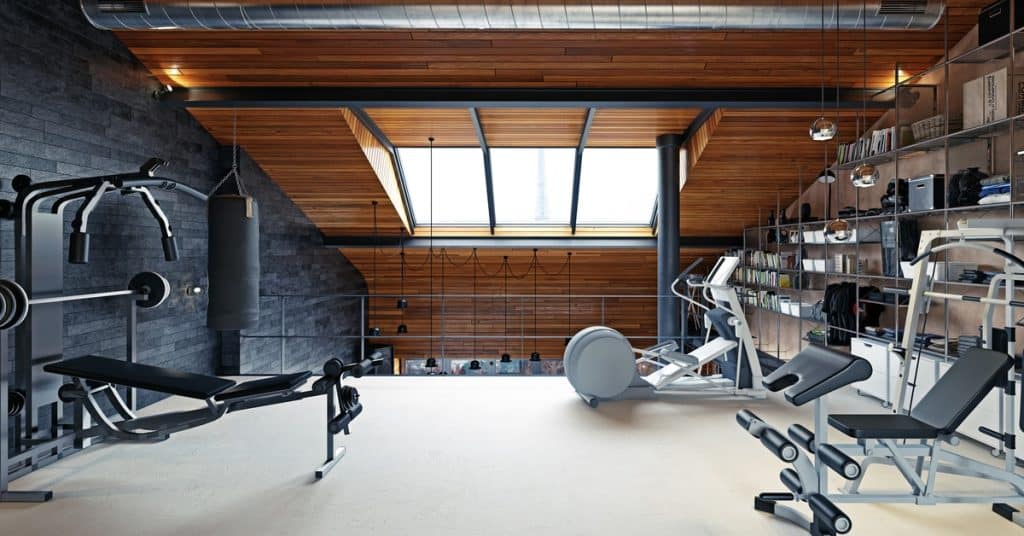A view of a home gym room in a loft-style attic with modern equipment and storage shelving on the wall.