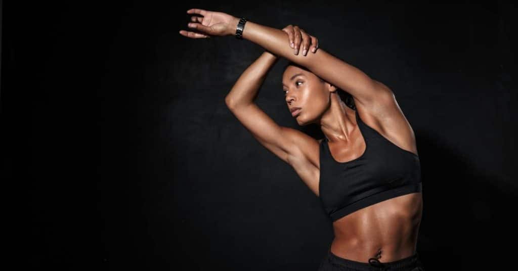 Athletic woman stretching her arms during a fitness workout against a dark background in a studio setting.